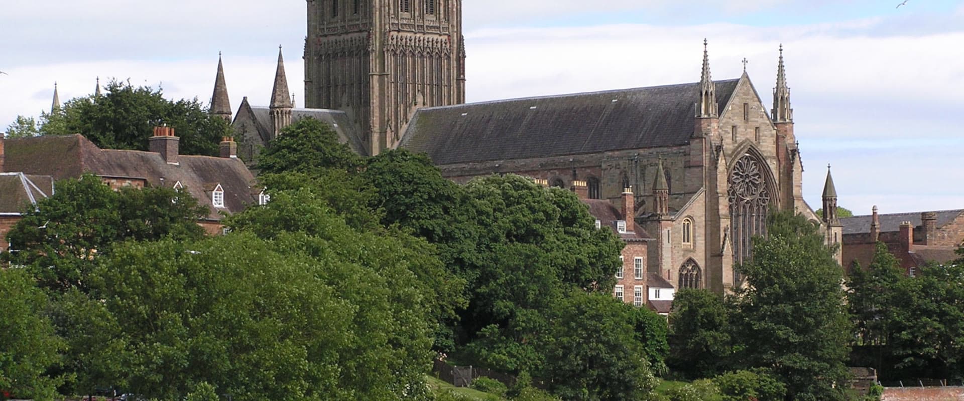 Worcester Cathedral rising above the River Severn on a bright day, with a passenger boat moored below