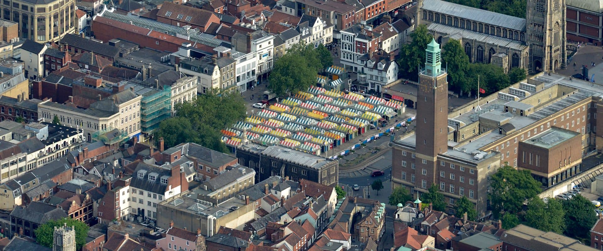 Aerial view of Norwich Market's striped stalls with City Hall's clock tower and St Peter Mancroft church behind