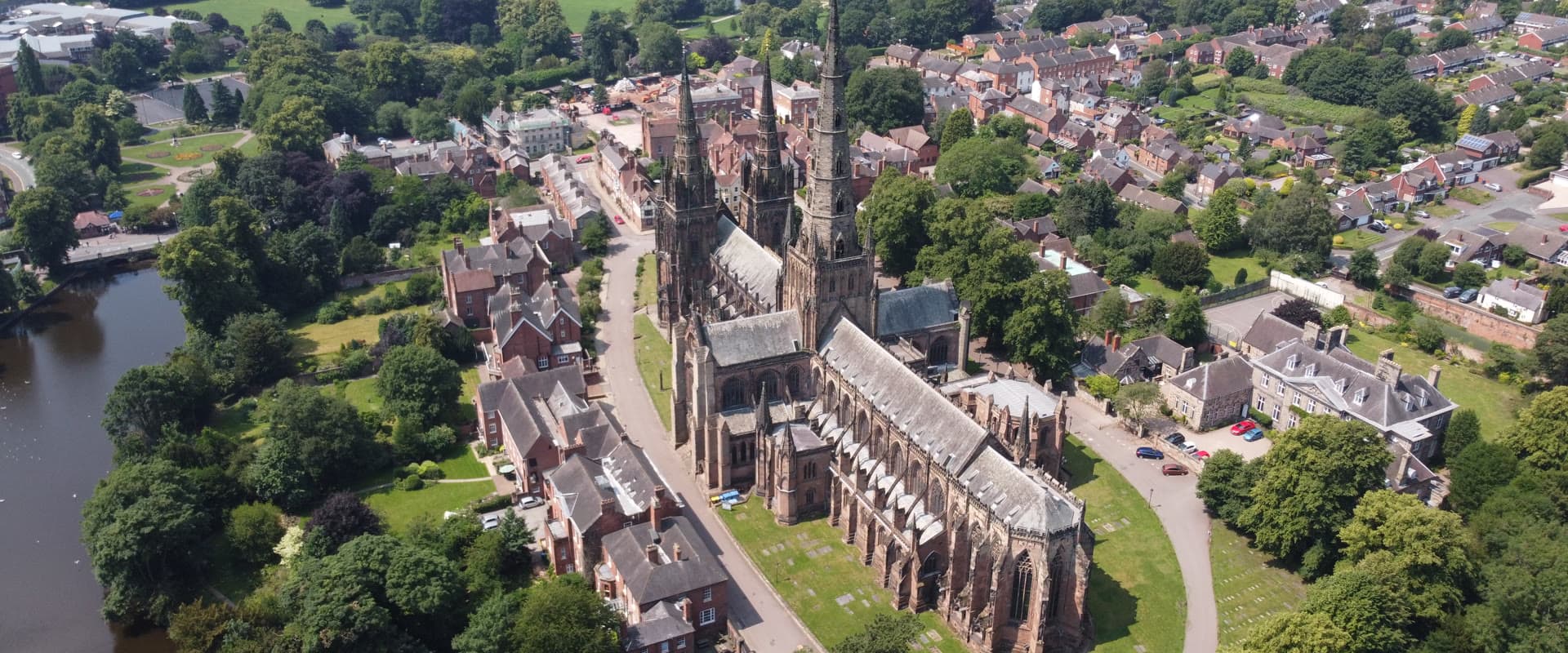 Aerial view of Lichfield Cathedral's three spires on a bright day, with the town and Minster Pool below