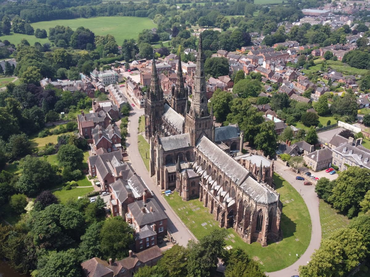 Aerial view of Lichfield Cathedral's three spires on a bright day, with the town and Minster Pool below