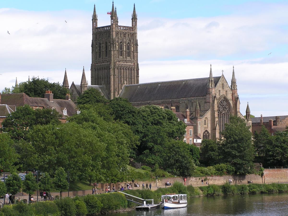 Worcester Cathedral rising above the River Severn on a bright day, with a passenger boat moored below